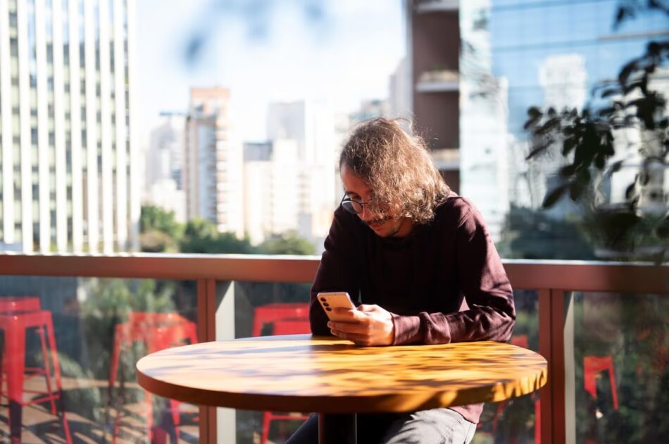 DREX: uma pessoa sentada em uma mesa e mexendo no celular.