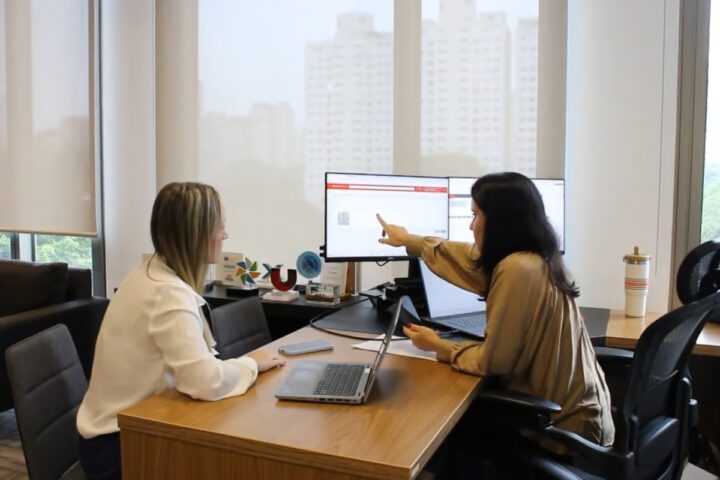 Gestão financeira: mulheres conversando em um escritório e analisando dados no computador.